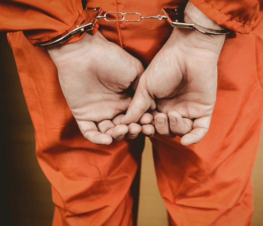 Two hands wearing handcuffs behind the back of someone wearing orange